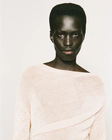 Portrait of a Black man wearing a textured light-colored top against a plain white background by Damien Krisl.