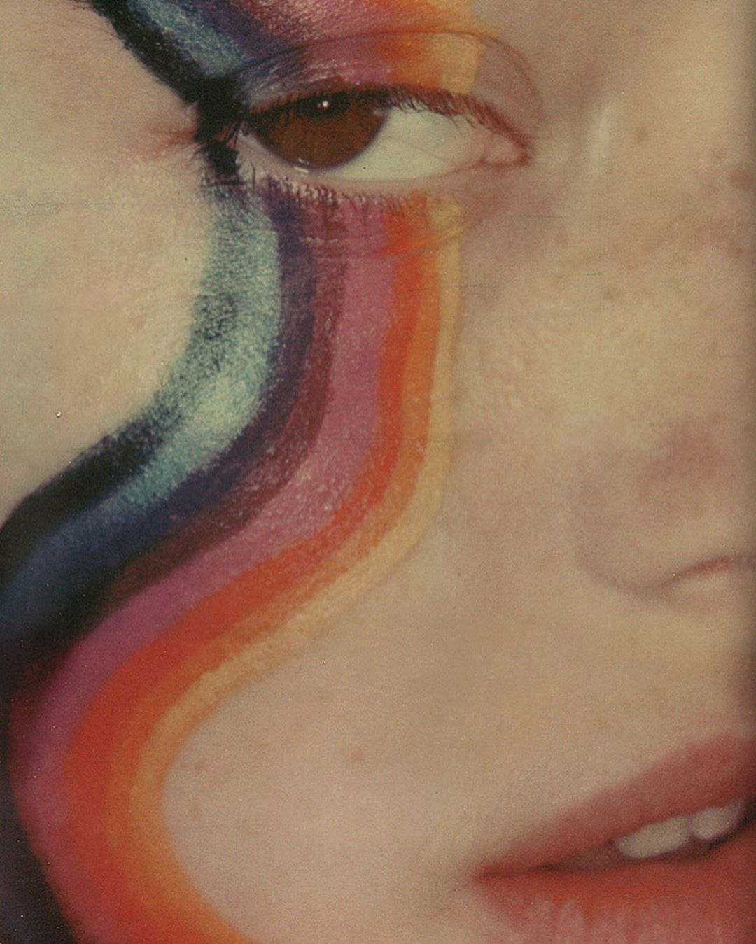 Close-up of a face with colorful rainbow makeup extending from the eye. Beauty shot with vibrant, blended colors.