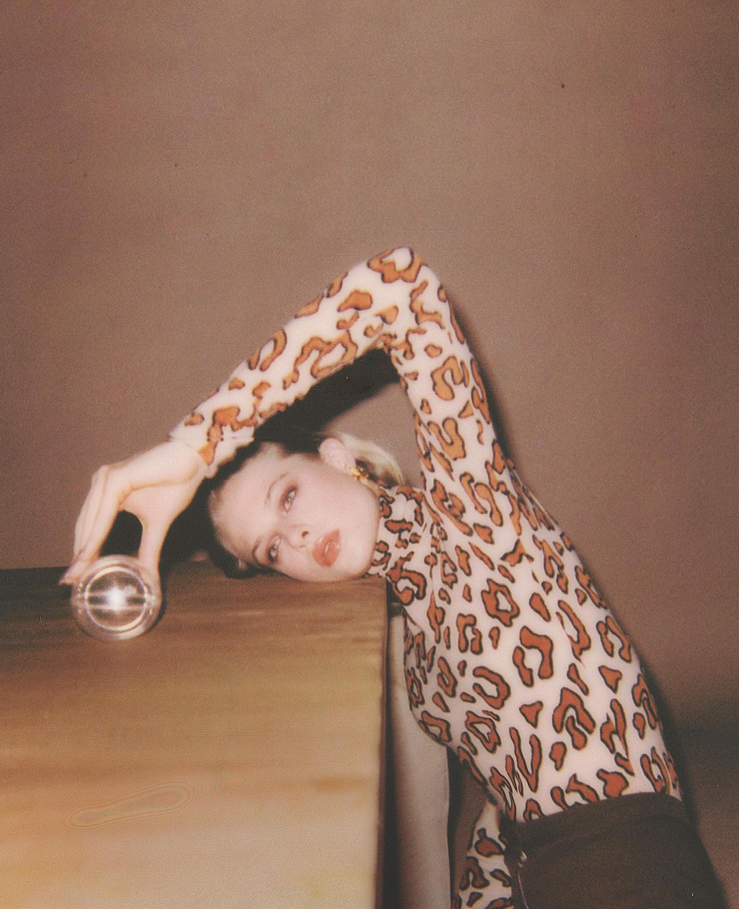 Woman in leopard print top leans on table with glass orb. Fashion portrait with soft lighting and warm tones.