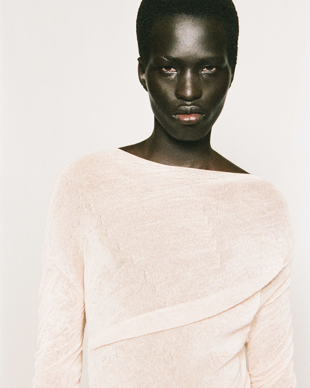 Portrait of a Black woman in a light pink knit top against a white background, facing the camera with a serious expression.