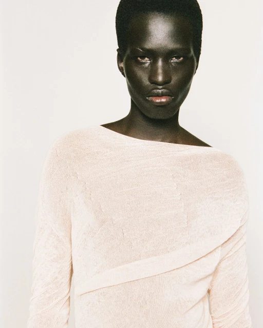 Portrait of a Black woman in a light pink knit top against a white background, facing the camera with a serious expression.