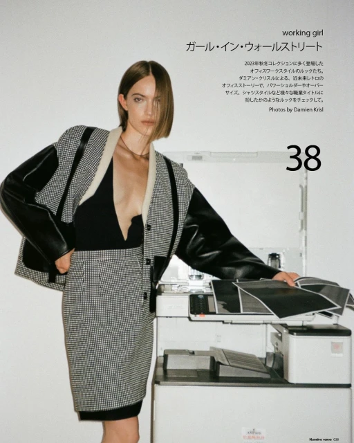 A woman poses in a patterned blazer and skirt next to an office printer in a fashion editorial with natural lighting and a modern aesthetic.