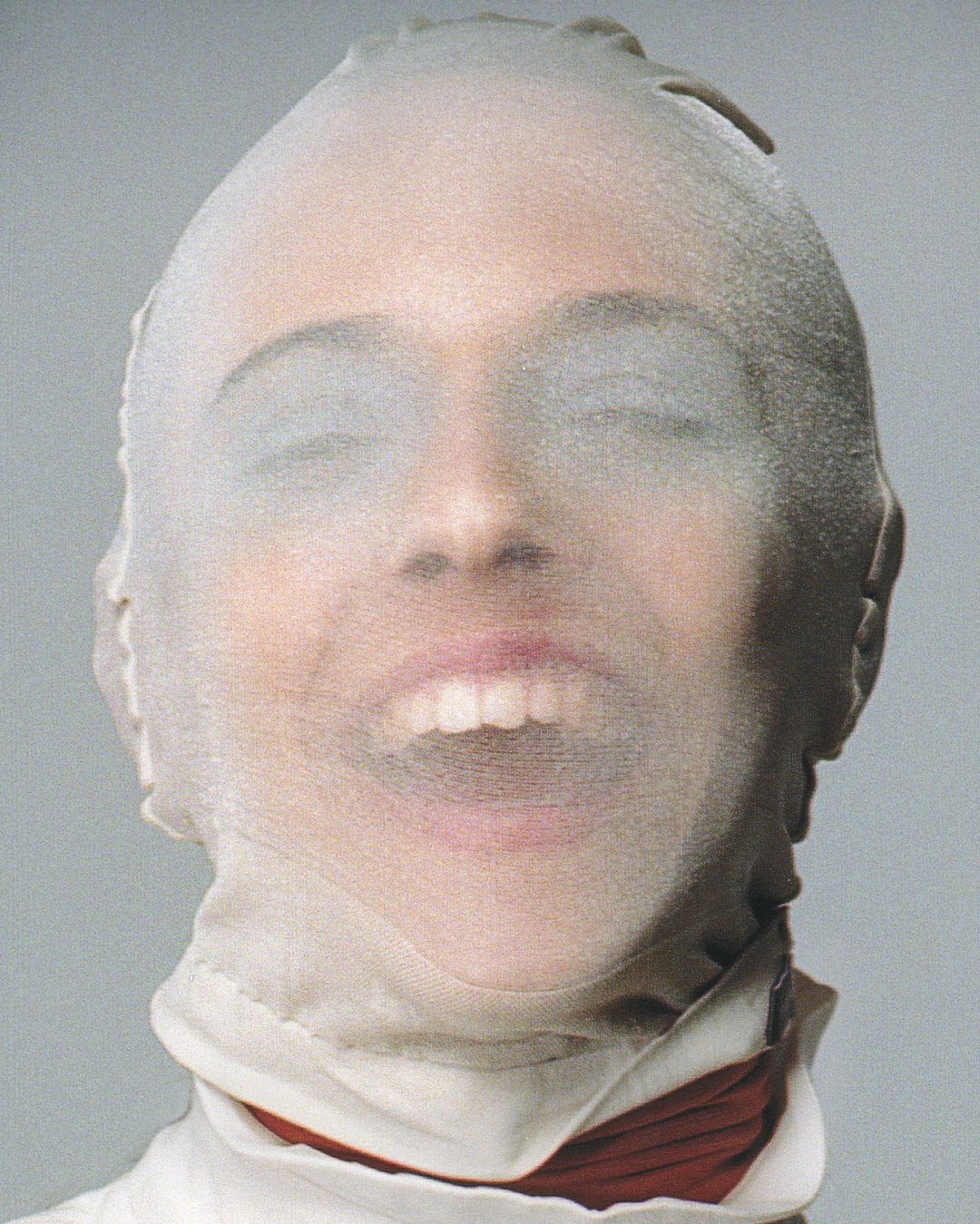 Woman with semi-opaque white nylon stocking over her head and face, eyes closed, and mouth open, studio lighting, and neutral background.