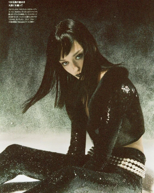 Elegant woman with dark hair poses indoors wearing black sequined pants and a matching long-sleeved top, accessorized with a pearl belt.