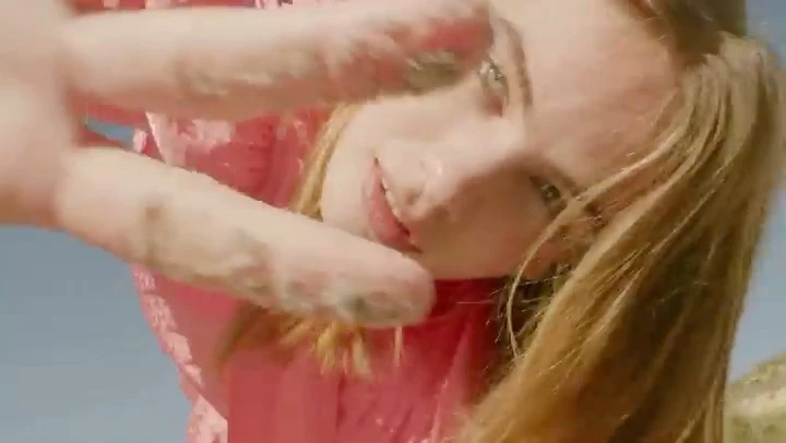 Close-up of a woman in a pink floral dress reaching towards the camera under a clear blue sky