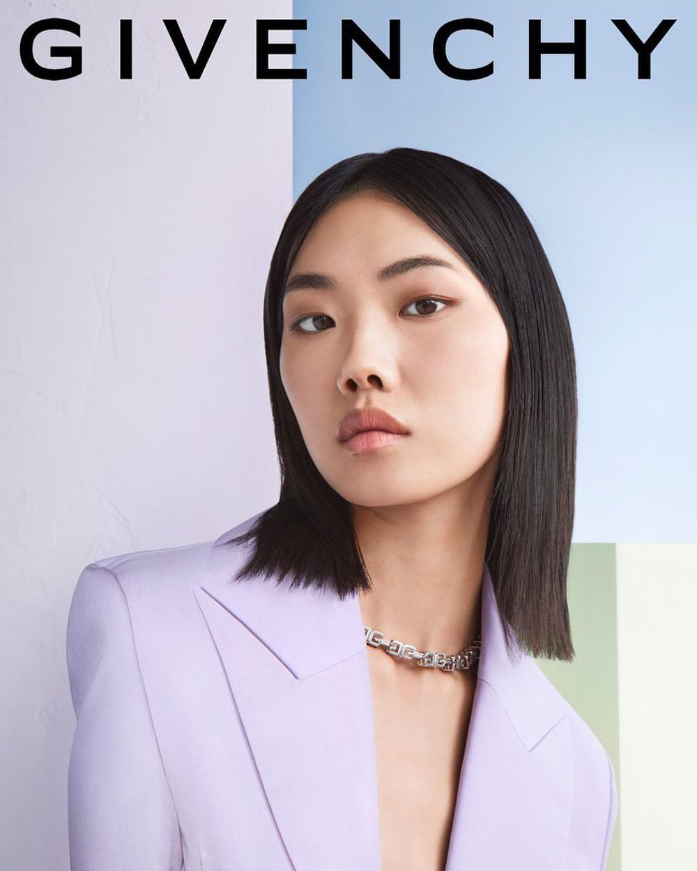 Asian woman in lilac blazer with silver chain necklace poses in front of a pastel backdrop for a fashion advertisement.