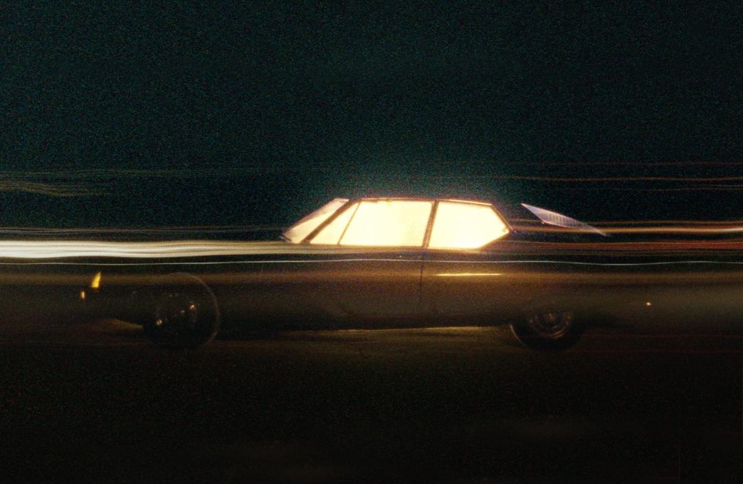 Vintage car in motion at night with long exposure, capturing light trails in dark setting; Automotive industry aesthetic.
