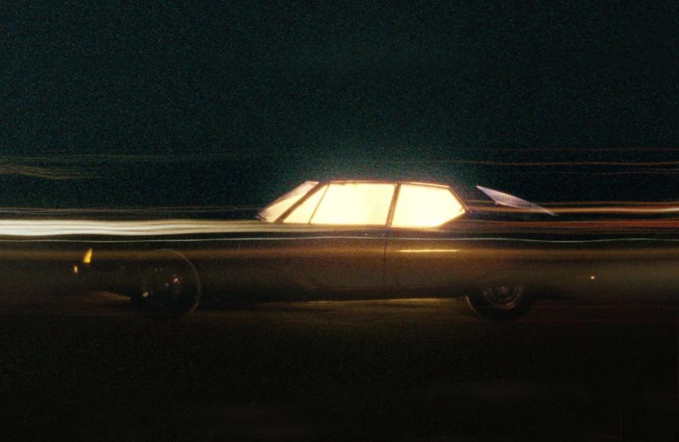 Vintage car in motion at night with long exposure, capturing light trails in dark setting; Automotive industry aesthetic.