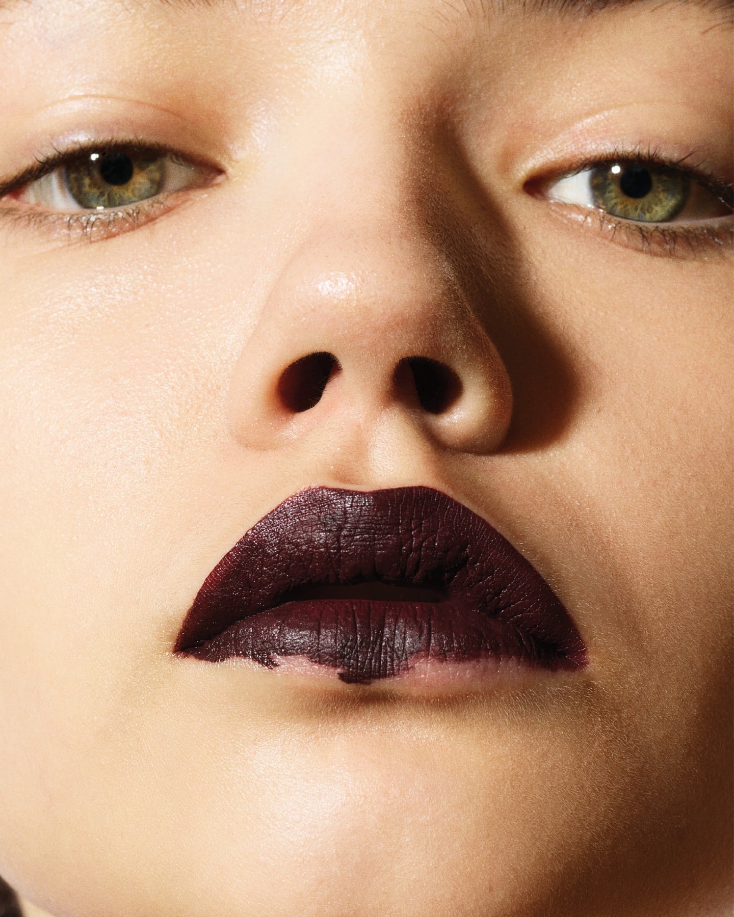 Close-up shot of a woman's face showcasing bold, dark purple lipstick. Her skin is fair, and she has light green eyes. 