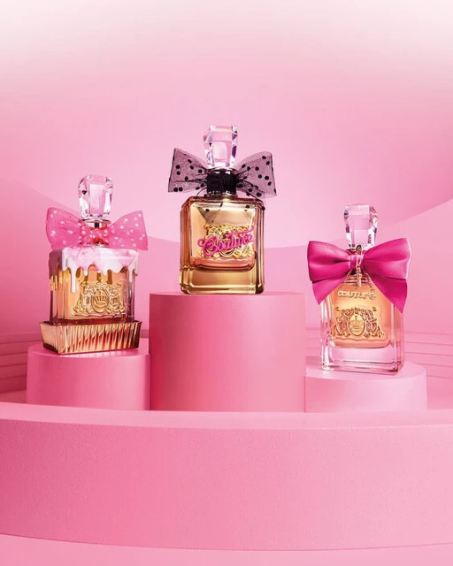 Three Juicy Couture perfume bottles displayed on pink platforms with pink bows, against a pink background.