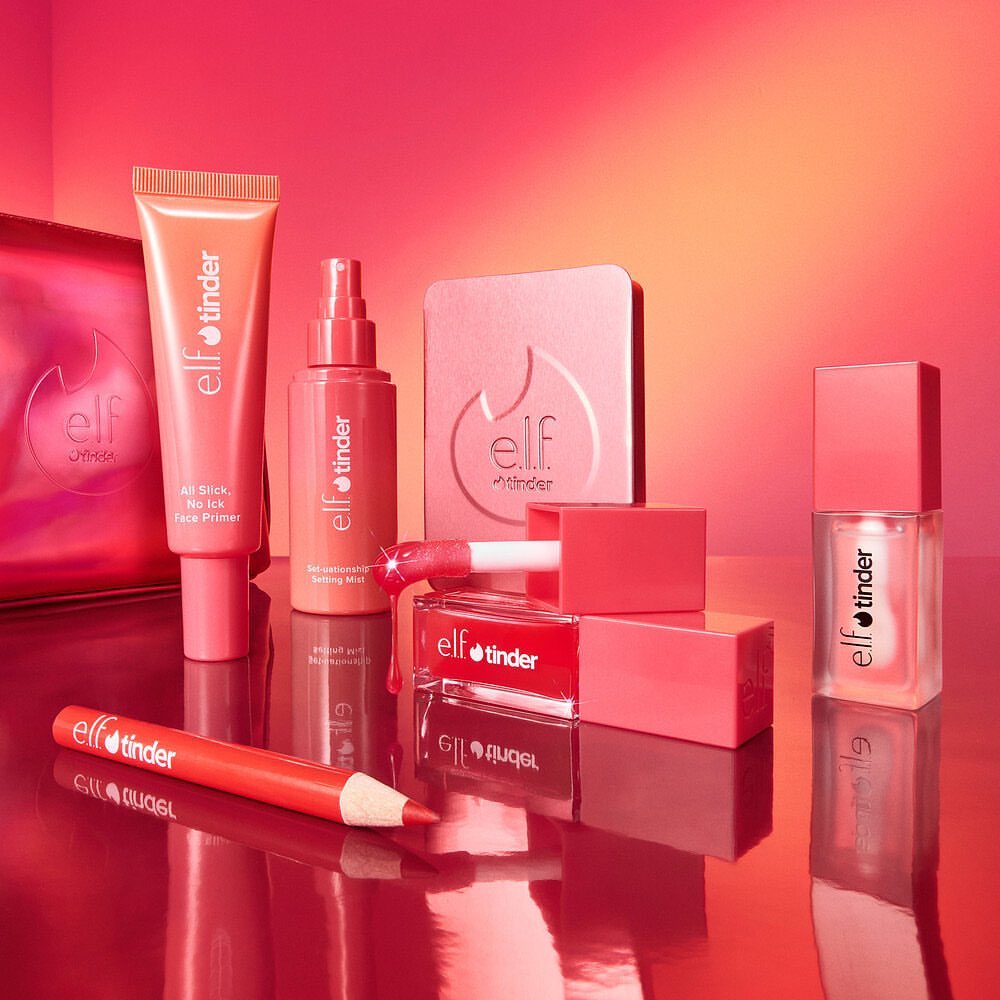 Still life studio shot of e.l.f. Cosmetics 'tinder' product line, including primer, setting spray, powder, lip gloss, lip stick, and liner.