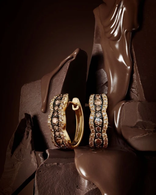 Close-up of gold hoop earrings encrusted with brown and white diamonds, artfully arranged on textured chocolate for a luxurious feel.