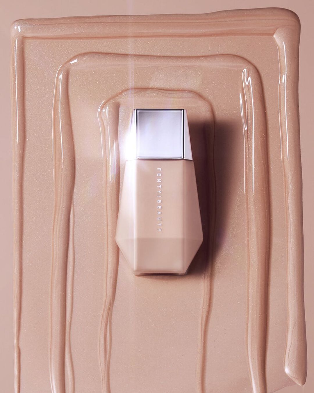 Fenty Beauty foundation bottle on a neutral background with liquid foundation swirls. Beauty product shot with a modern cosmetic design.