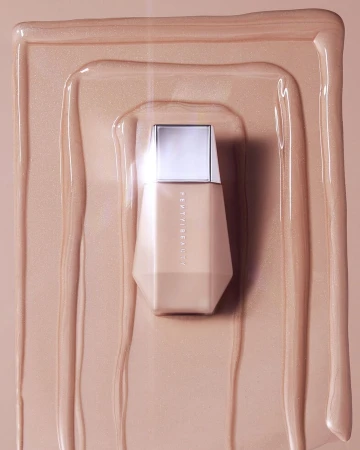 Fenty Beauty foundation bottle on a neutral background with liquid foundation swirls. Beauty product shot with a modern cosmetic design.