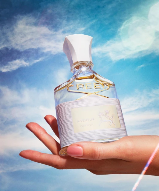 Creed Aventus perfume bottle held in hand against a blue sky background. Beauty shot for product marketing.