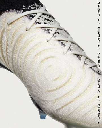 Close-up studio shot of a white Nike Phantom GX soccer cleat with laces and black detailing against a white backdrop. 