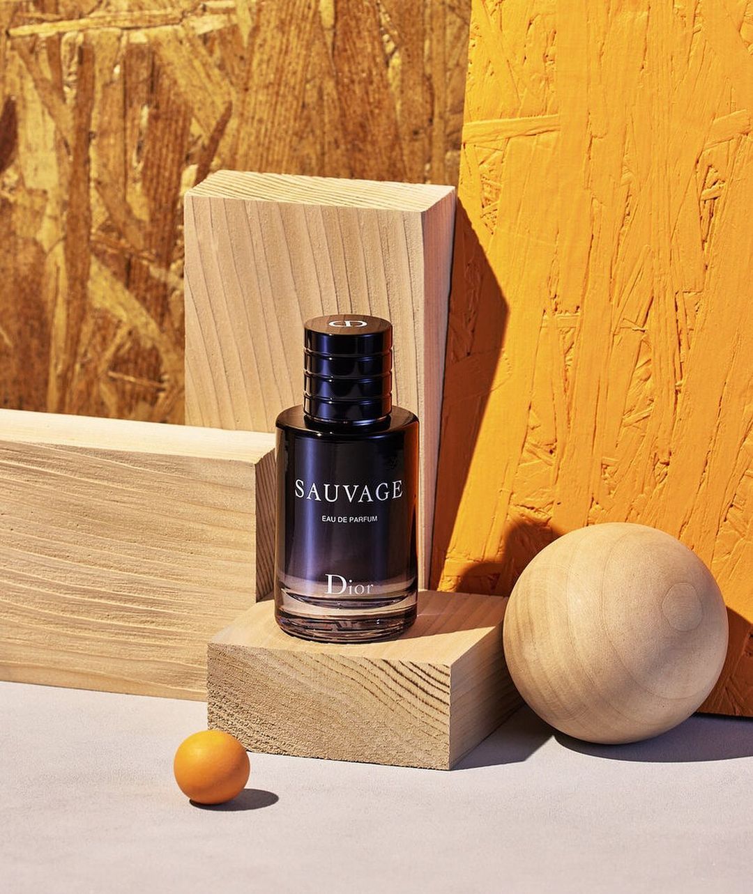 Dior Sauvage Eau de Parfum bottle stands prominently amid light wood blocks and a wooden sphere against a striking patterned backdrop.