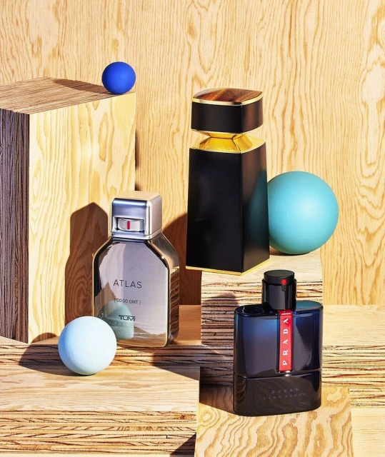 Three perfume bottles by Prada and Tumi are displayed on a wooden surface with pastel spheres. Elegant fragrance still life.