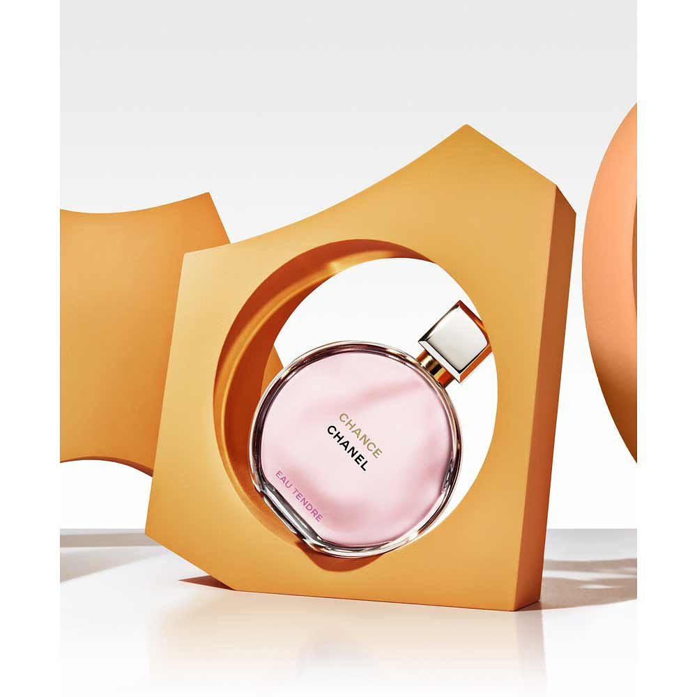 Chanel Chance Eau Tendre perfume bottle on a white surface, framed by an abstract geometric figure of orange and light tones.