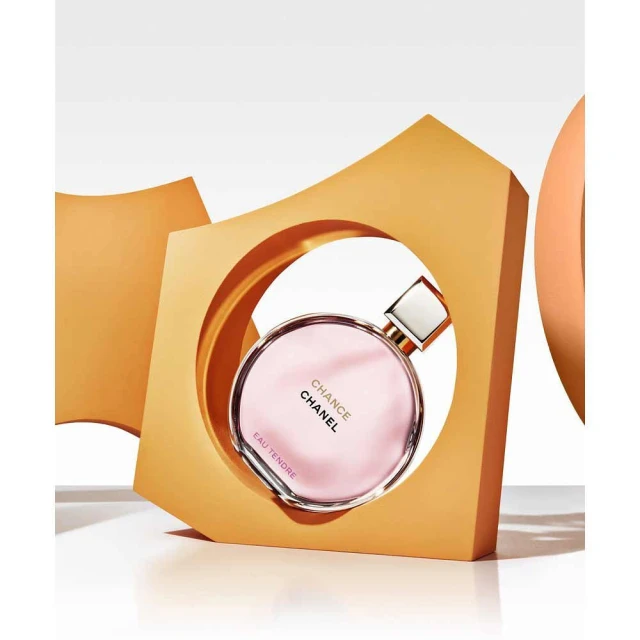Chanel Chance Eau Tendre perfume bottle on a white surface, framed by an abstract geometric figure of orange and light tones.