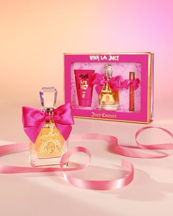 Viva La Juicy perfume gift set with pink ribbon and packaging. The product is displayed against a soft peach and pink gradient background.