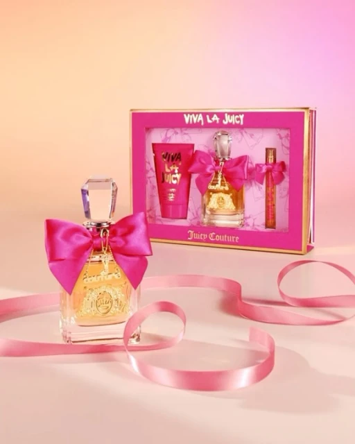 Viva La Juicy perfume gift set with pink ribbon and packaging. The product is displayed against a soft peach and pink gradient background.