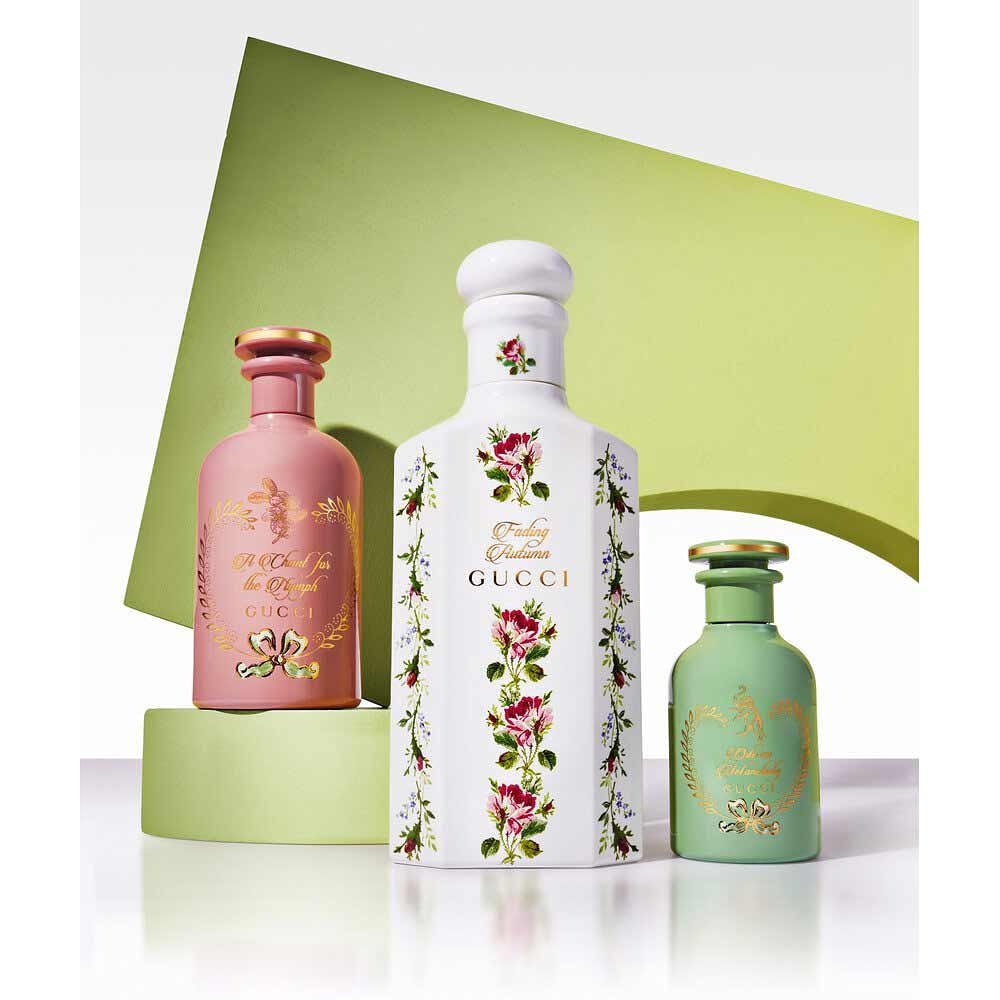 Three Gucci perfume bottles of different colors and sizes are displayed on a green platform with a backdrop of a lime green shape.