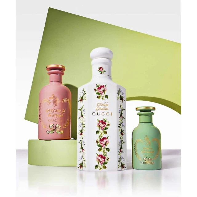 Three Gucci perfume bottles of different colors and sizes are displayed on a green platform with a backdrop of a lime green shape.