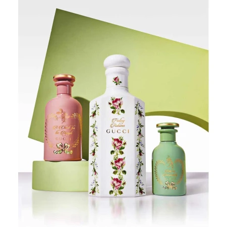 Three Gucci perfume bottles of different colors and sizes are displayed on a green platform with a backdrop of a lime green shape.