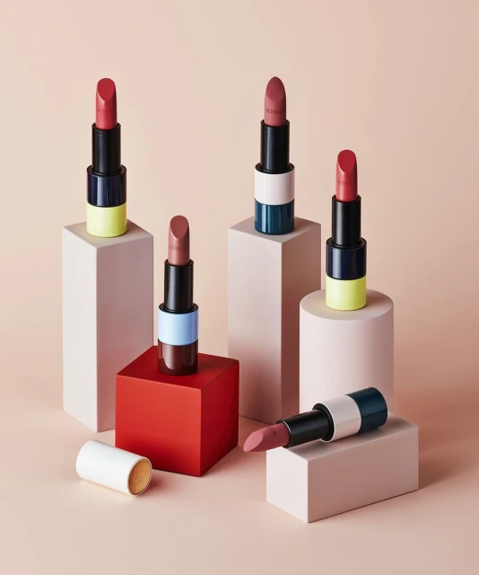 Group of Hermès lipsticks in varying shades arranged on geometric pedestals in a studio shot. Focus on colors and product presentation.