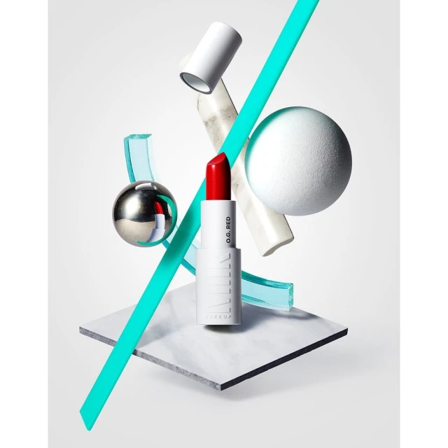 Milk Makeup red lipstick on a white marble surface with blue and white geometric shapes against a white background in a studio shot.