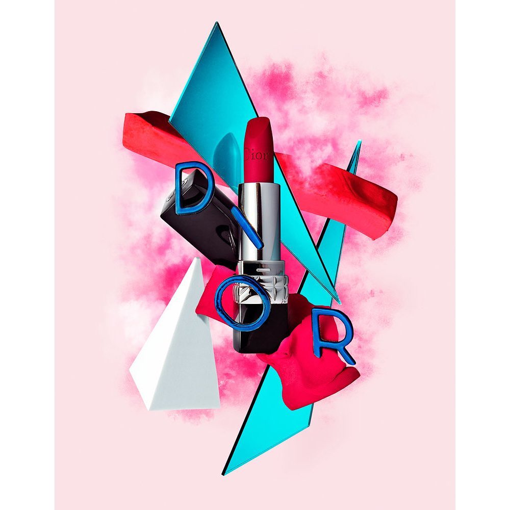 A red Dior lipstick tube is surrounded by geometric shapes and the letters D-I-O-R on a gradient light pink and white background.