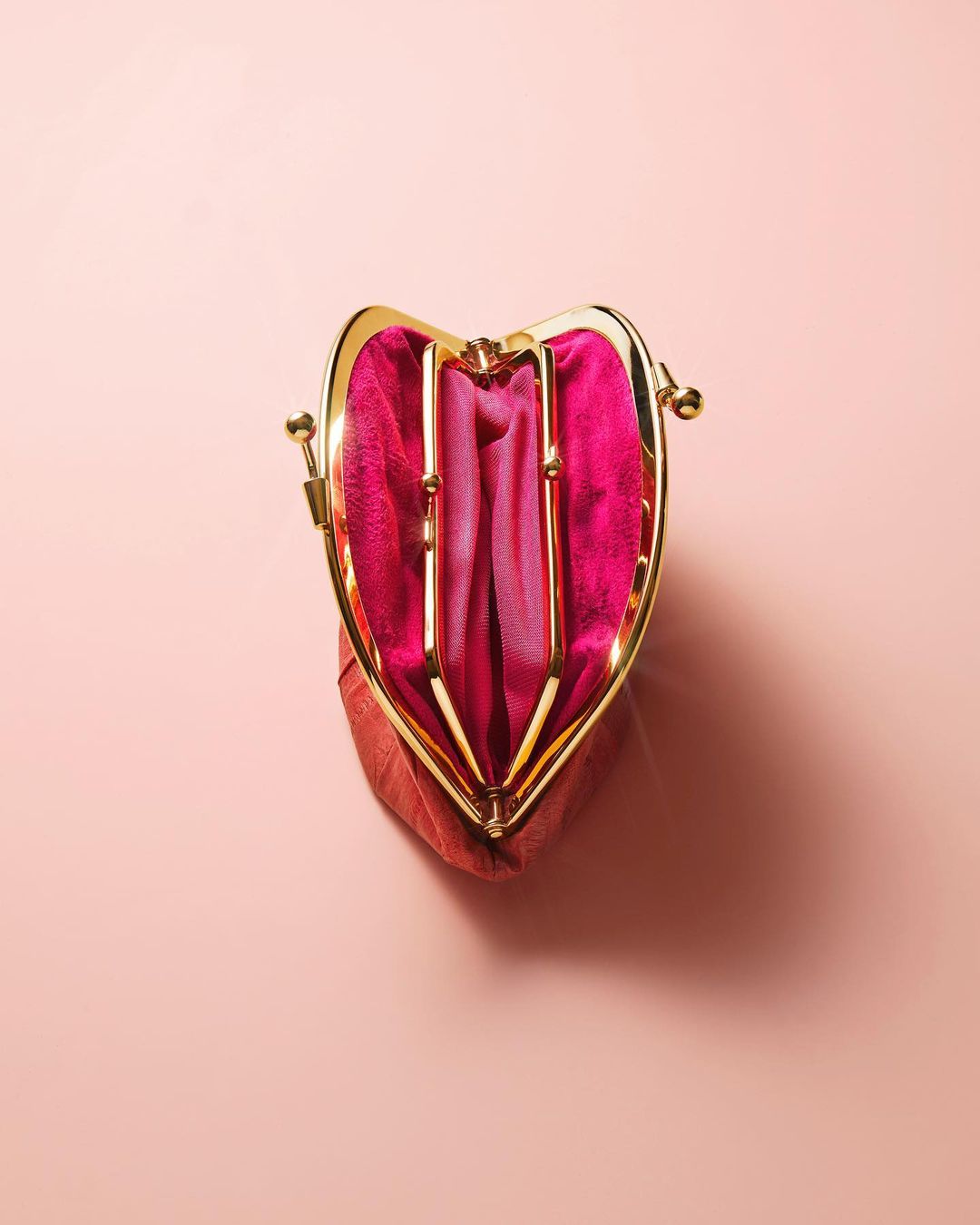 Studio shot of an open coin purse, featuring pink satin lining and a gold metal clasp, set against a pastel pink background.