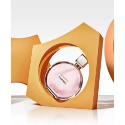 Round glass perfume bottle with pink liquid framed by orange geometric props on a white background