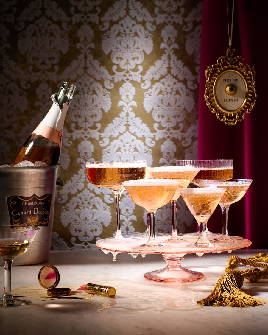 Celebratory image featuring champagne glasses, an ice bucket with a champagne bottle, and vintage-style props against a damask wallpaper backdrop.