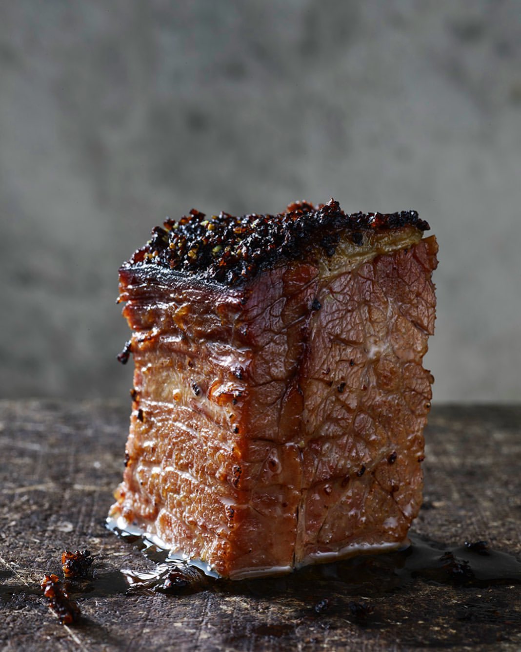 Studio shot of a single cube of glazed and roasted pork belly on a dark surface, with dark background, close-up shot, food photography.