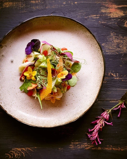Overhead shot of artistic salad plate with edible flowers and microgreens on dark wooden table. Food and Beverage, studio lighting.