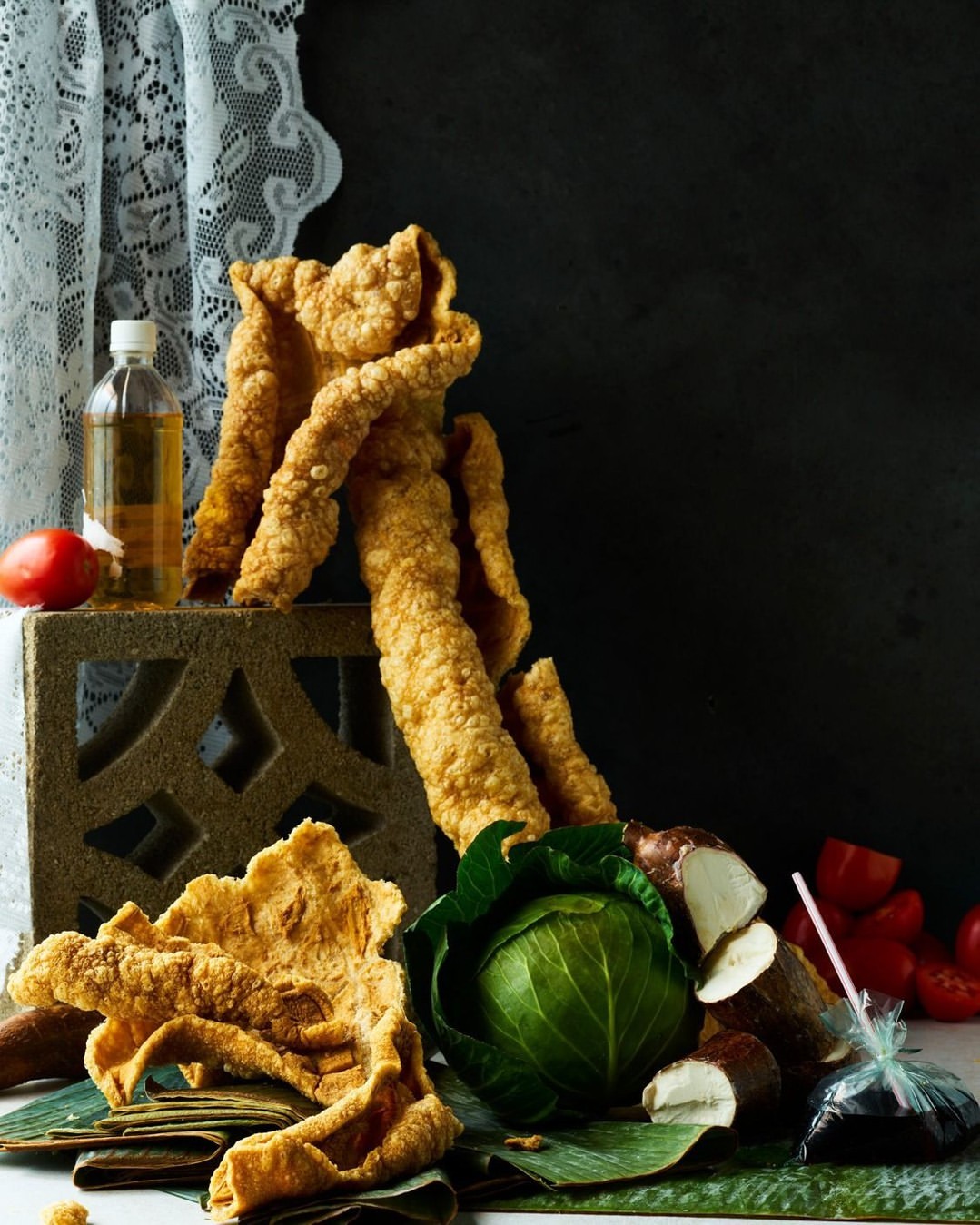 Close-up studio shot of golden crispy fried food with cabbage, tomato, and oil bottle on a table against dark background.