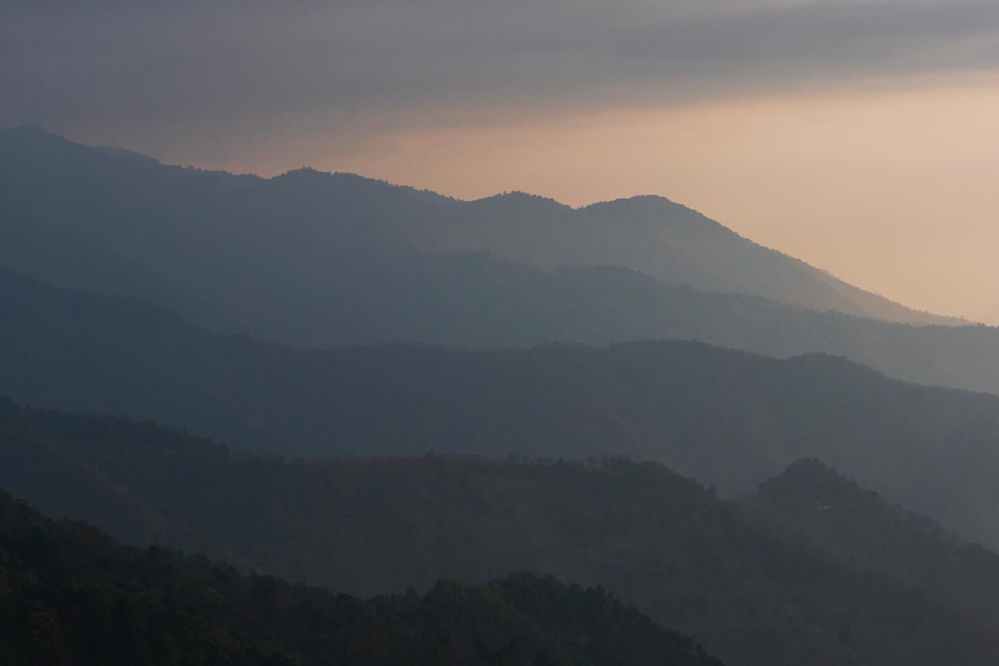 Scenic view of distant mountain range with dramatic cloudy sky, creating a hazy, atmospheric landscape at dusk or dawn.