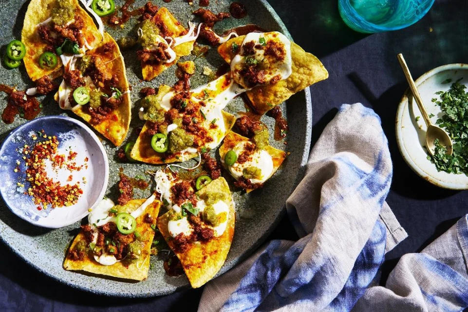 Overhead shot of loaded nachos on a speckled plate with red pepper flakes, cilantro, and a blue and white linen napkin.