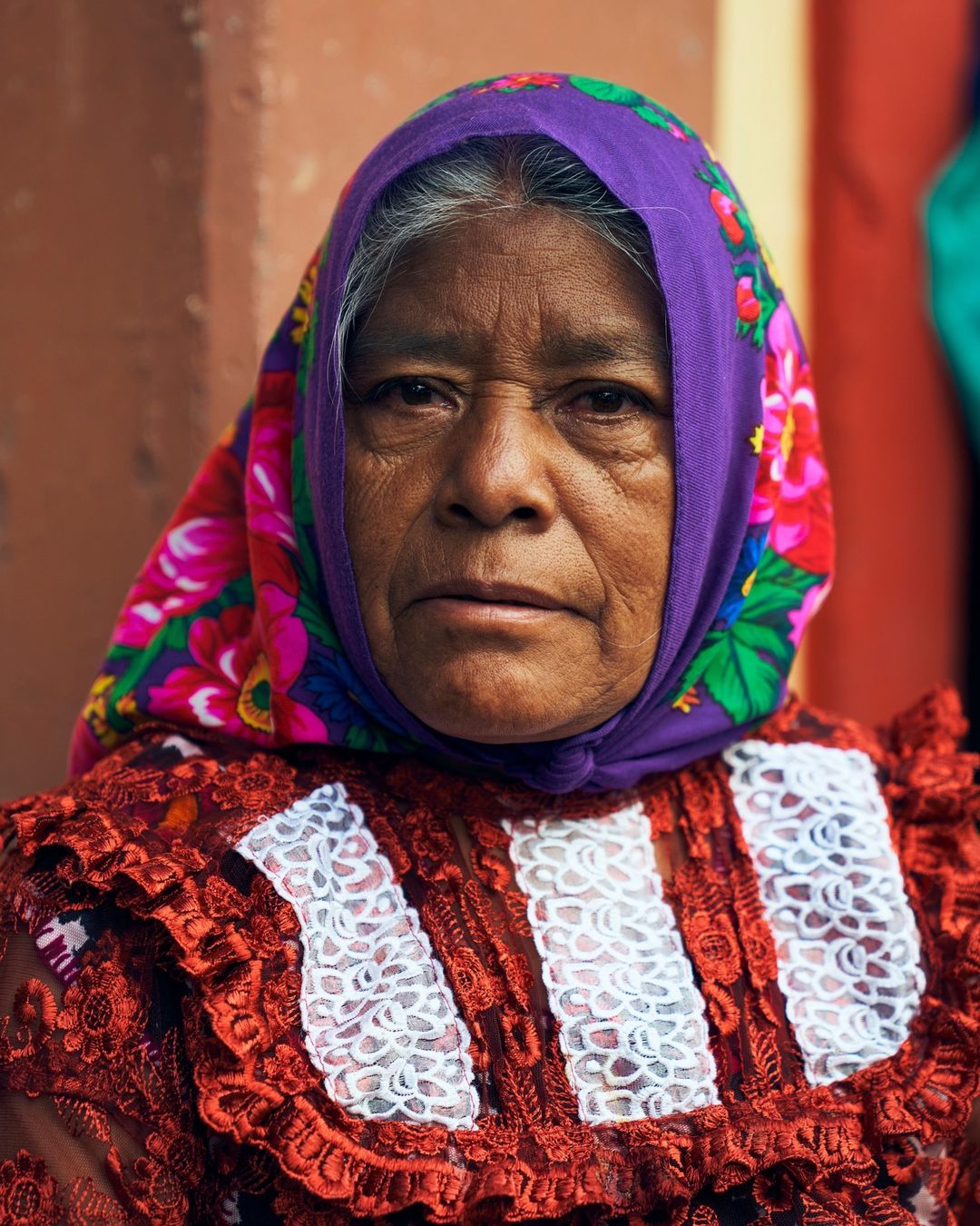 Close-up portrait of an Indigenous woman in traditional red dress and purple floral headscarf, capturing cultural heritage and portraiture.