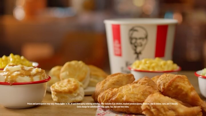 Still life of fried chicken, mashed potatoes with gravy, corn, mac and cheese, and biscuits arranged on a wooden surface.