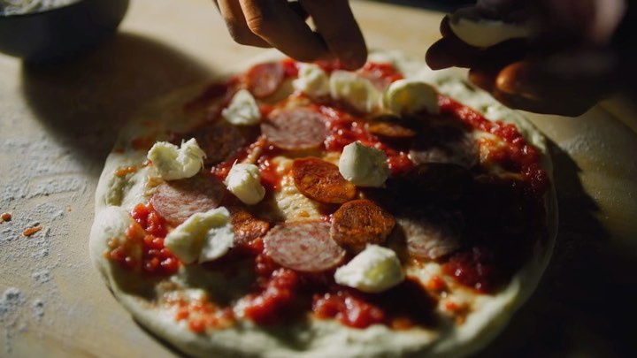 Close-up of a pepperoni pizza being topped with mozzarella balls, showcasing ingredients and preparation, illuminated by focused lighting.