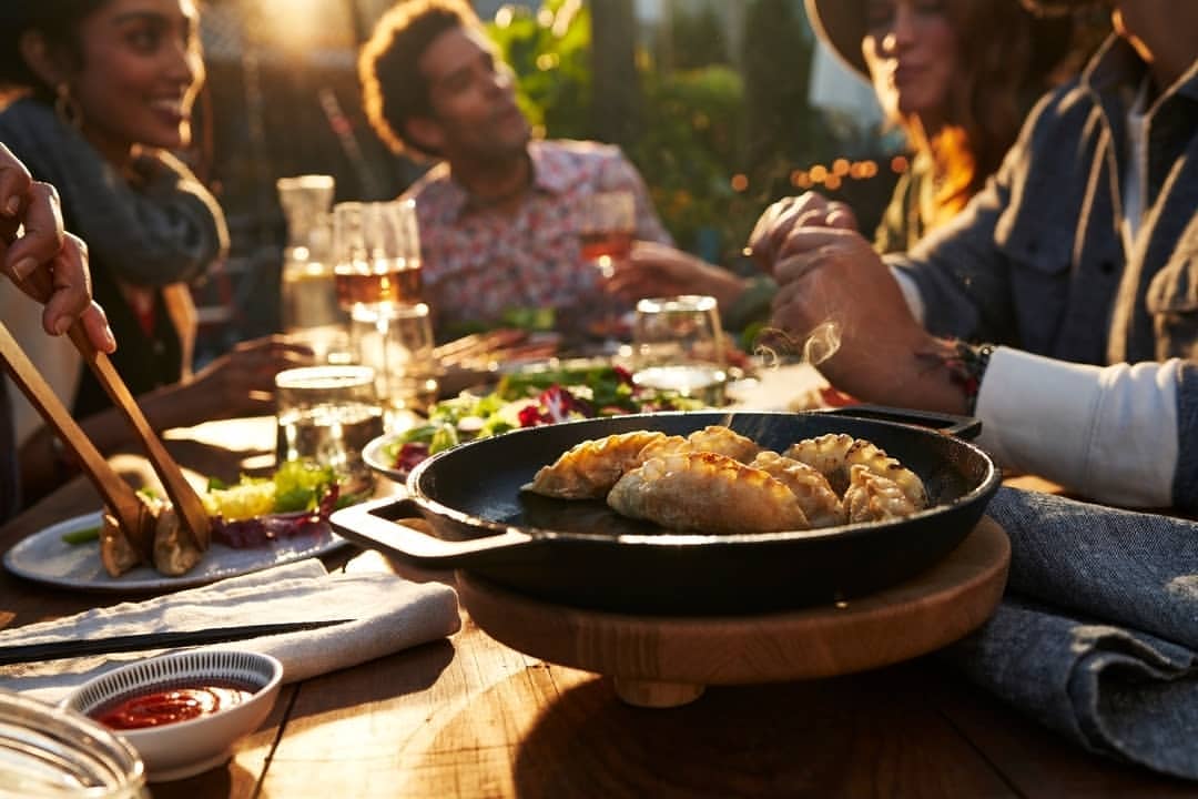Outdoor dining scene features a group of people enjoying food, including dumplings, with natural light and a warm, inviting atmosphere.