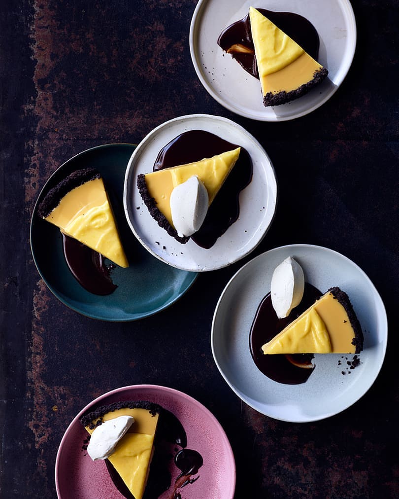 Overhead shot of plates with slices of pie, chocolate sauce, and dollops of cream; dark background; food photography for a food blog.
