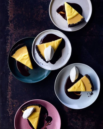 Overhead shot of plates with slices of pie, chocolate sauce, and dollops of cream; dark background; food photography for a food blog.