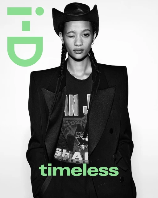 A portrait of a young adult female with braided hair, wearing a cowboy hat, black blazer, and graphic tee, with the i-D logo visible.