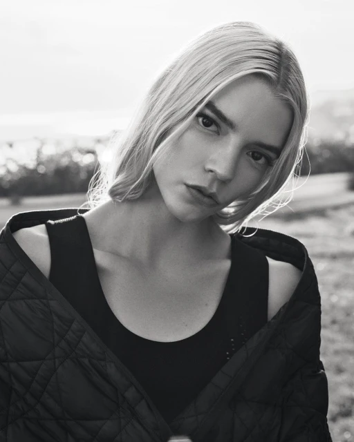 Black and white portrait of a woman with fair hair, wearing a dark top and quilted jacket, posing outdoors in natural light.
