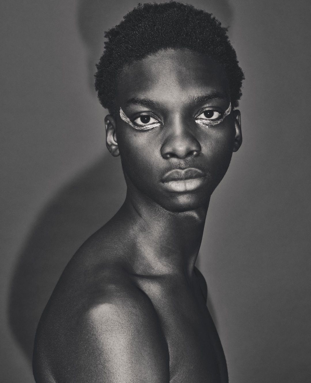 Close-up black and white portrait of a young Black man with painted eyeliner by Dan Jackson