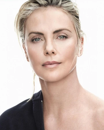 Close-up portrait of a blonde woman with a serious facial expression wearing a dark blue jacket against a bright white background.